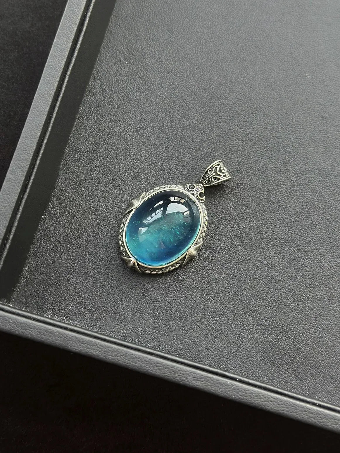 Devil blue aquamarine sterling silver pendant on a gray leather storage box