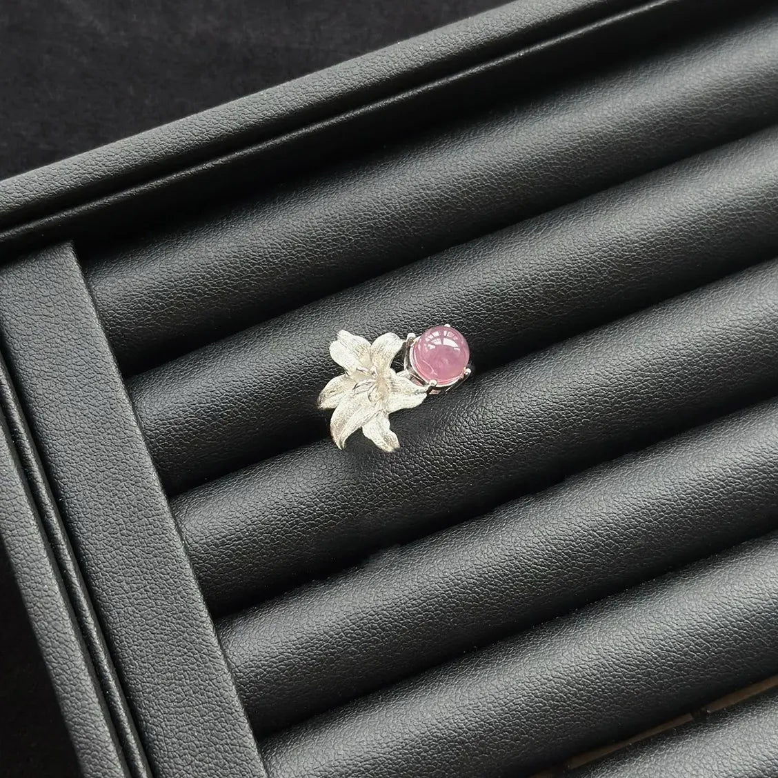 Silver Lily with a round pink quartz ring on a black leather surface