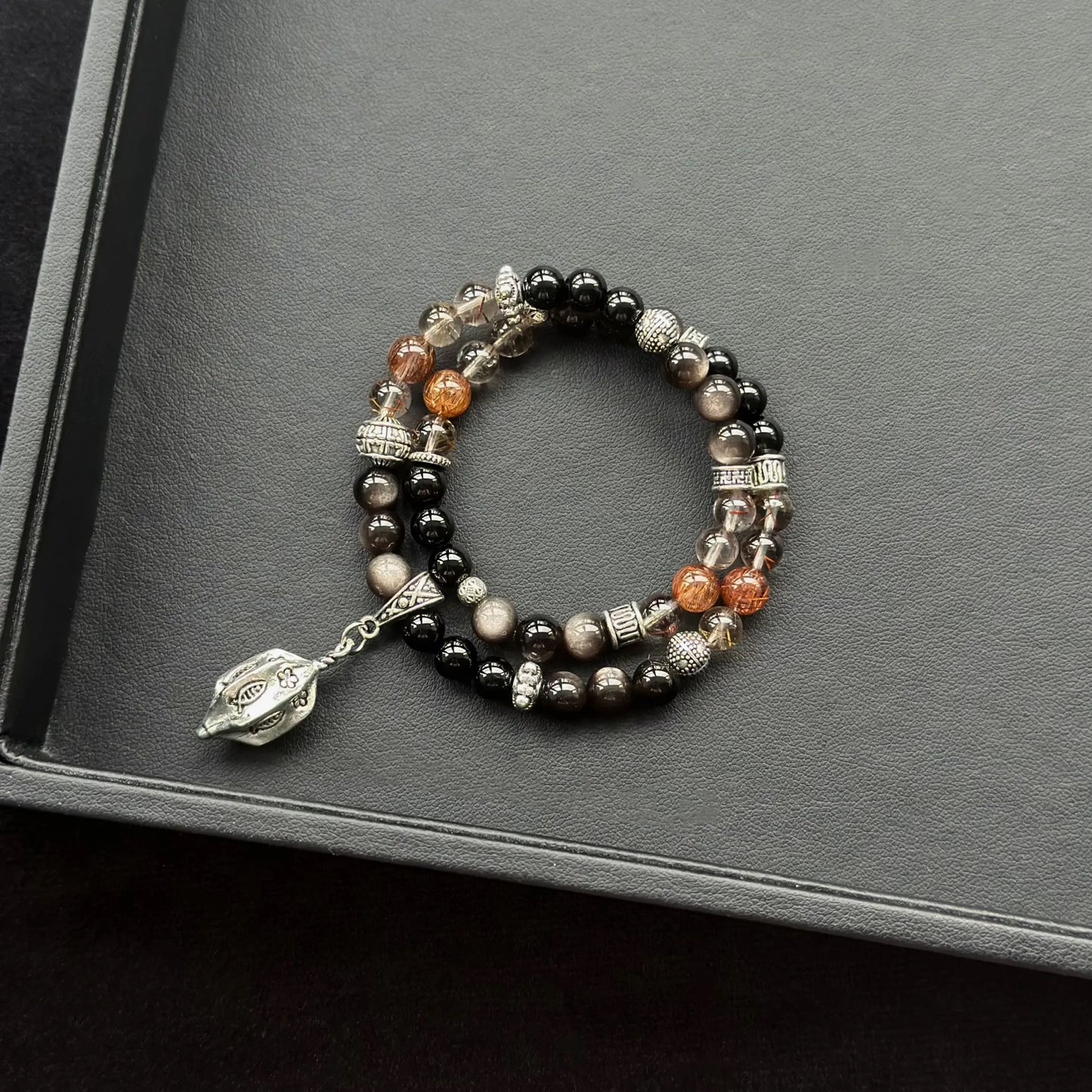 Black Agate & Black Obsidian & Red Copper Rutilated Quartz Bracelet on a dark surface