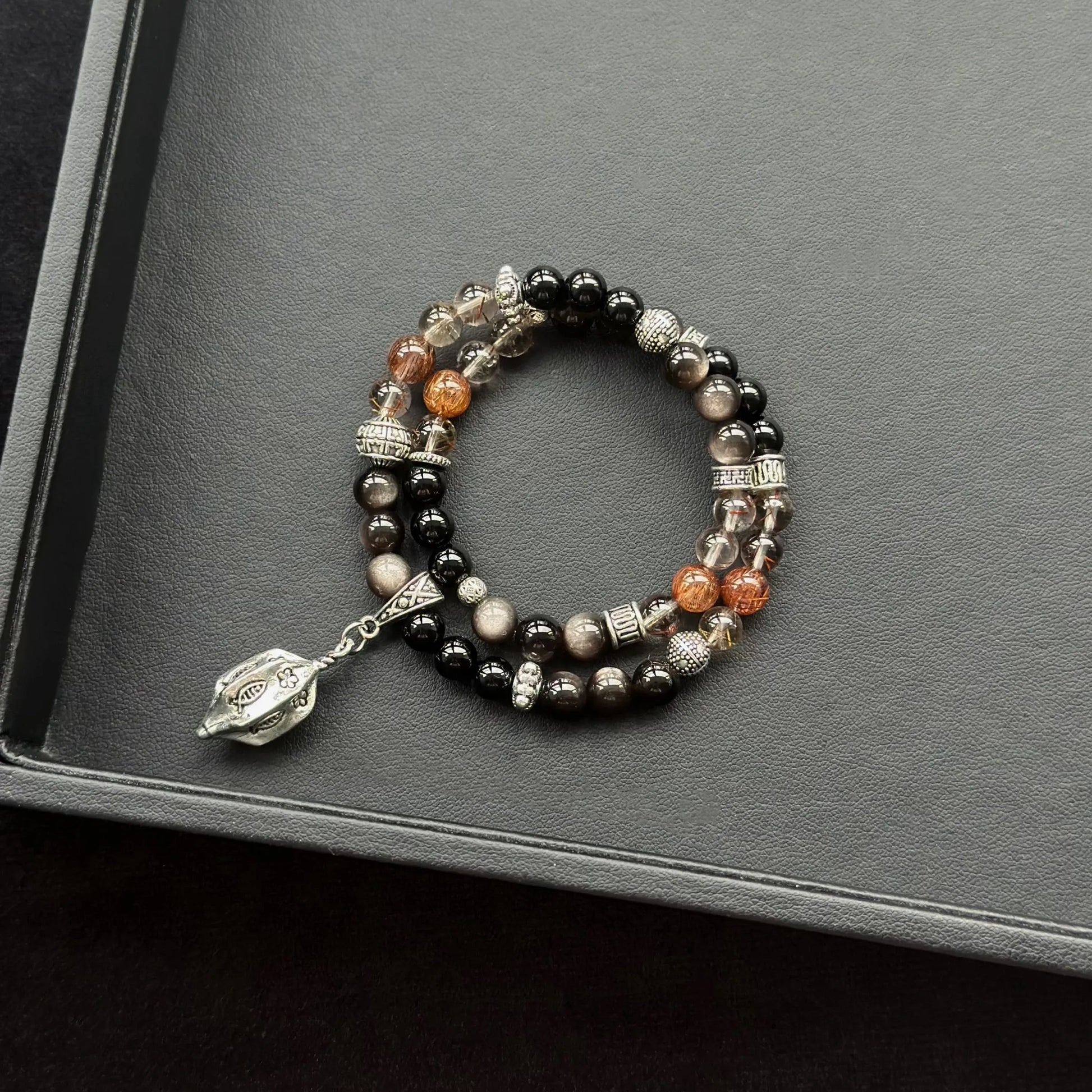 Black Agate & Black Obsidian & Red Copper Rutilated Quartz Bracelet on a dark surface