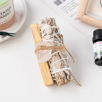 A healing crystal cleansing kit with a raw clear quartz point tied to a white sage stick for clarity and desk accessories.