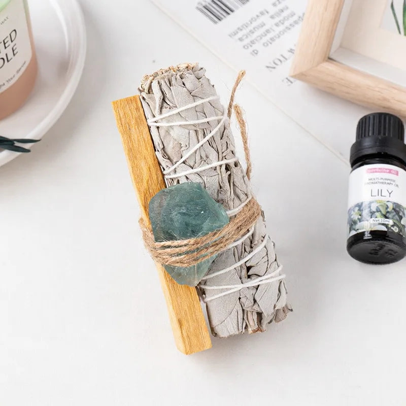 An aesthetic gemstone home accessory featuring a raw green fluorite crystal bundle tied to a white sage smudge stick.