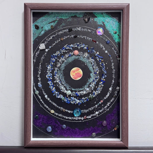 Full view of a handcrafted gemstone galaxy with crystal orbital rings in a wood frame.