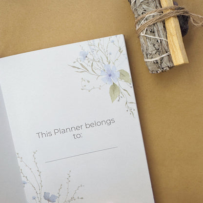An open celestial mindfulness journal showing an intricate gold foil sun constellation title page, surrounded by raw amethyst white sage smudge sticks.