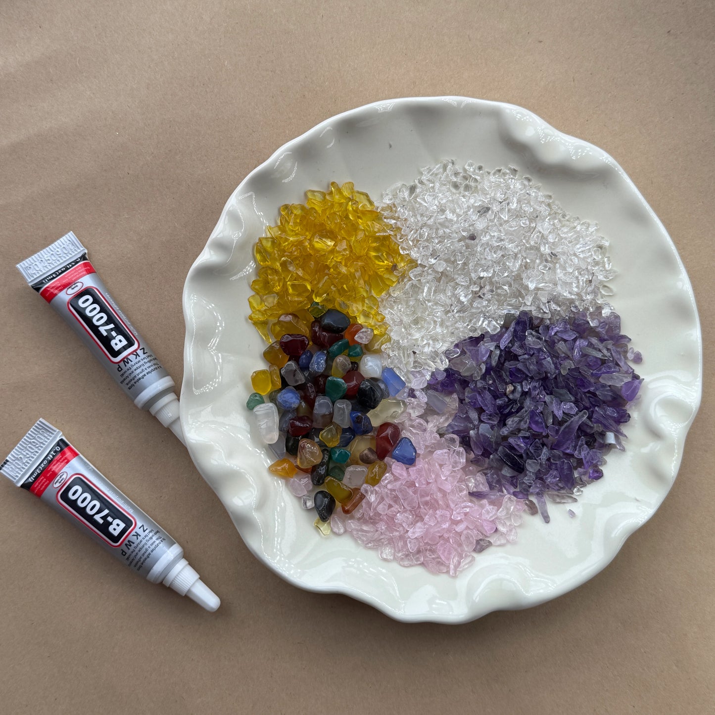A white plate holding mounds of natural Amethyst, Citrine, and Rose Quartz chips for crystal crafting.