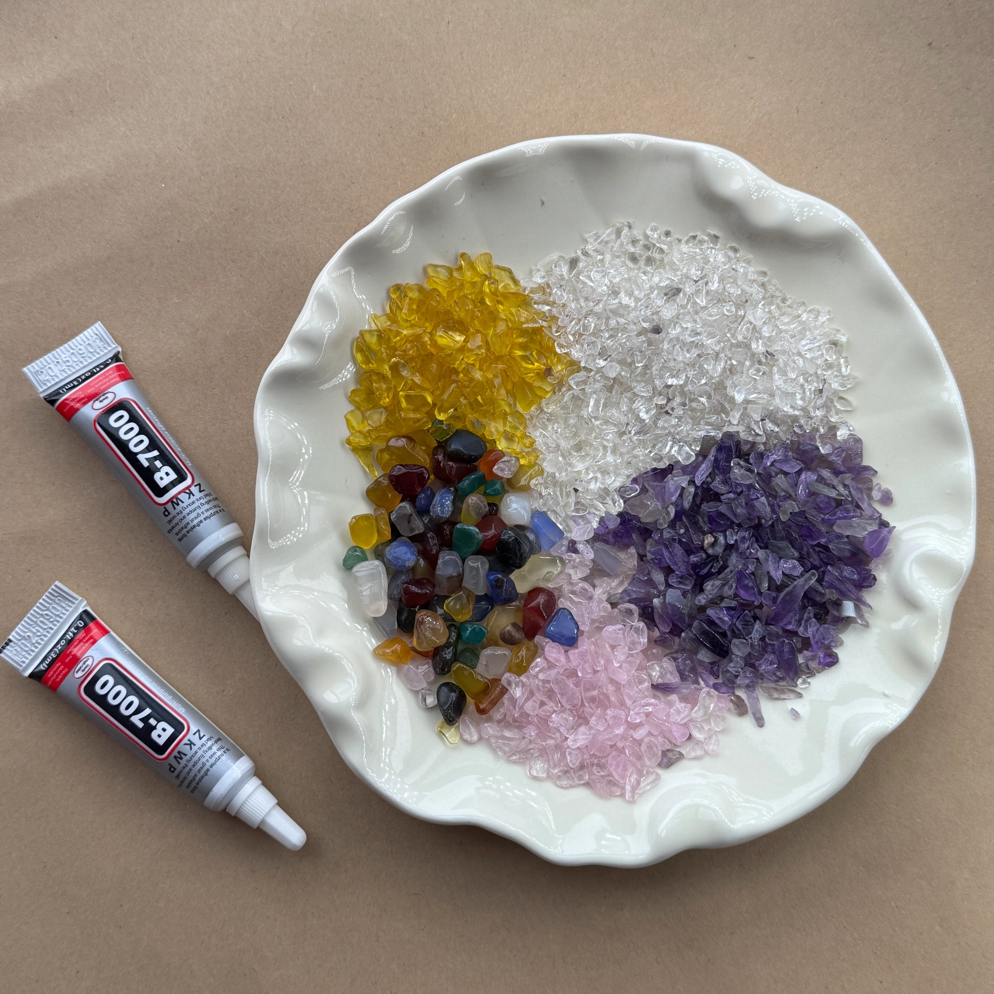 A white plate holding mounds of natural Amethyst, Citrine, and Rose Quartz chips for crystal crafting.