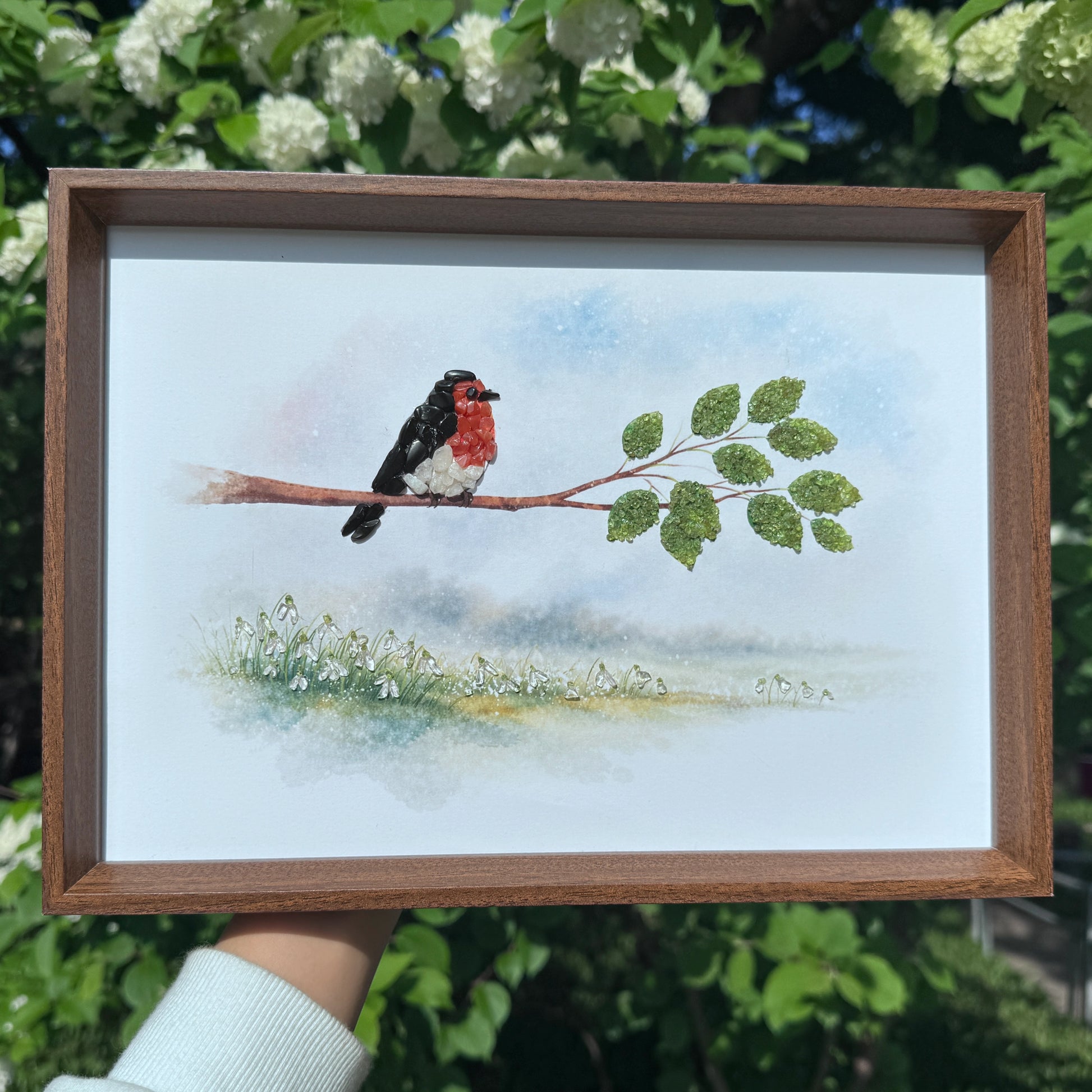 Lifestyle shot of a handmade crystal art frame held up against white spring flowers.