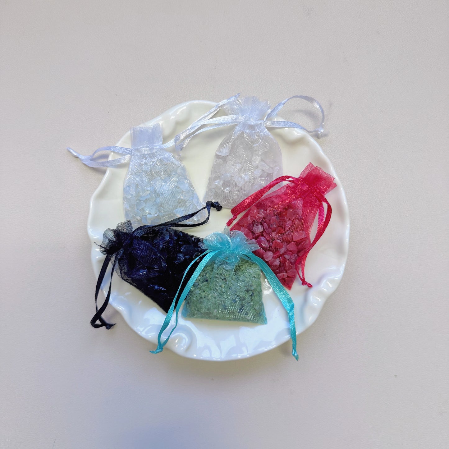 Five organza mesh bags filled with raw healing crystal chips—Clear Quartz, Opalite, Nanhong Agate, Obsidian, and Peridot—displayed neatly on a decorative plate.