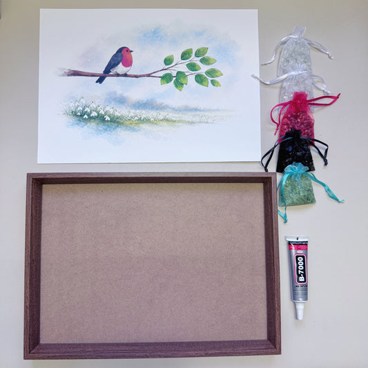 Flatlay view of the full Robin & Snowdrop Crystal Art Kit including wood-grain frame, canvas, 5 natural gemstones, and 15ml adhesive tube.