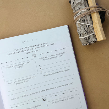 An open blank mindfulness journal on a desk styled with raw amethyst points, vintage elements, and desktop healing crystals.