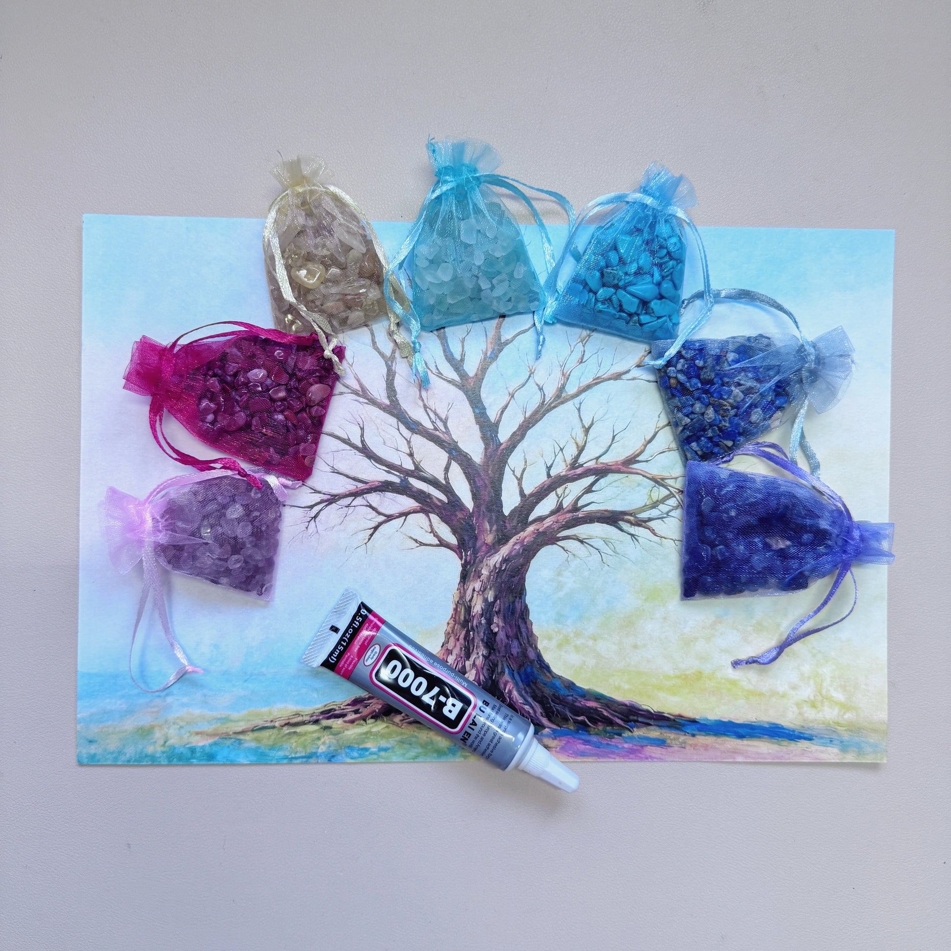 A4 Tree of Life canvas art surrounded by colorful raw gemstone chips and a tube of B-7000 glue for a mindful DIY diamond painting alternative.